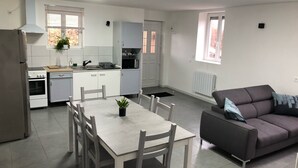 A modern kitchen with white cabinets, a dining table with chairs, and a gray sofa.