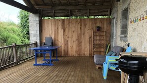 A covered outdoor deck with a blue table and chairs, a barbecue grill, and a wooden fence.