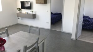 A modern room with a dining table, chairs, a mounted TV, and a bed with a blue patterned bedspread.