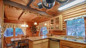 A wooden cabin interior with a dining area, kitchen, and large windows offering views of the surrounding forest. - The Bernstein Bear Cabin (Kings Beach)