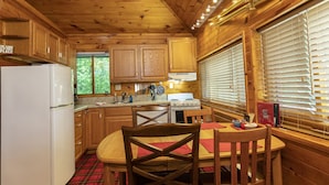 Una cocina estilo cabaña con armarios de madera, un refrigerador, estufa y una mesa de comedor con sillas.