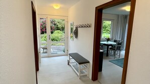 Un couloir avec un banc, un porte-manteau et un coin repas visible à travers une porte ouverte.