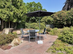 Un patio al aire libre con una mesa, sillas, una sombrilla grande y una parrilla.