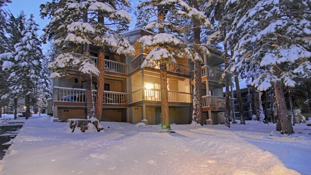 A multi-story building with balconies, surrounded by snow-covered trees. - Vidor Village (Kings Beach)