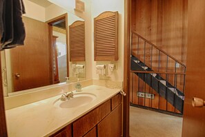 A bathroom with a large mirror, wooden cabinets, a sink, and a staircase with a railing. - Vidor Village (Kings Beach)