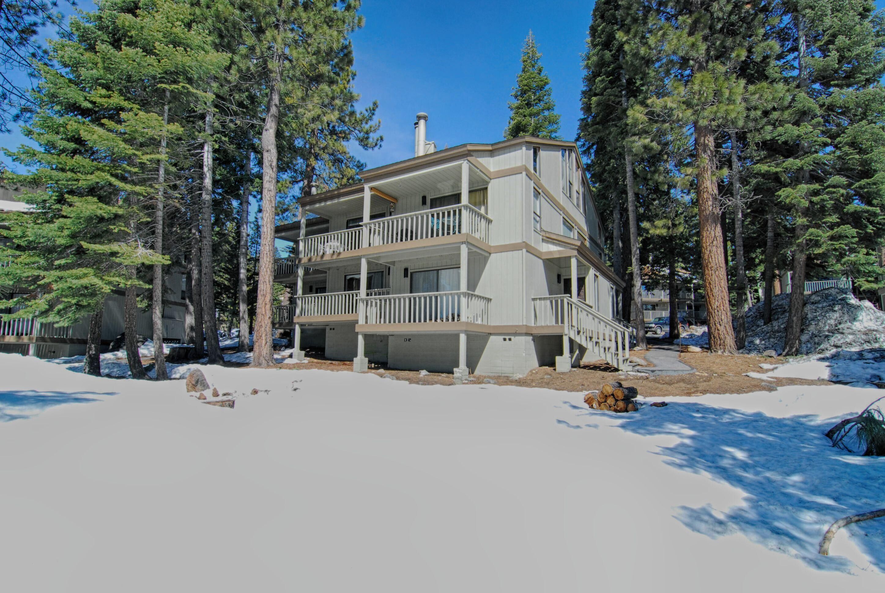 A multi-story building with balconies, surrounded by tall pine trees and snow on the ground.