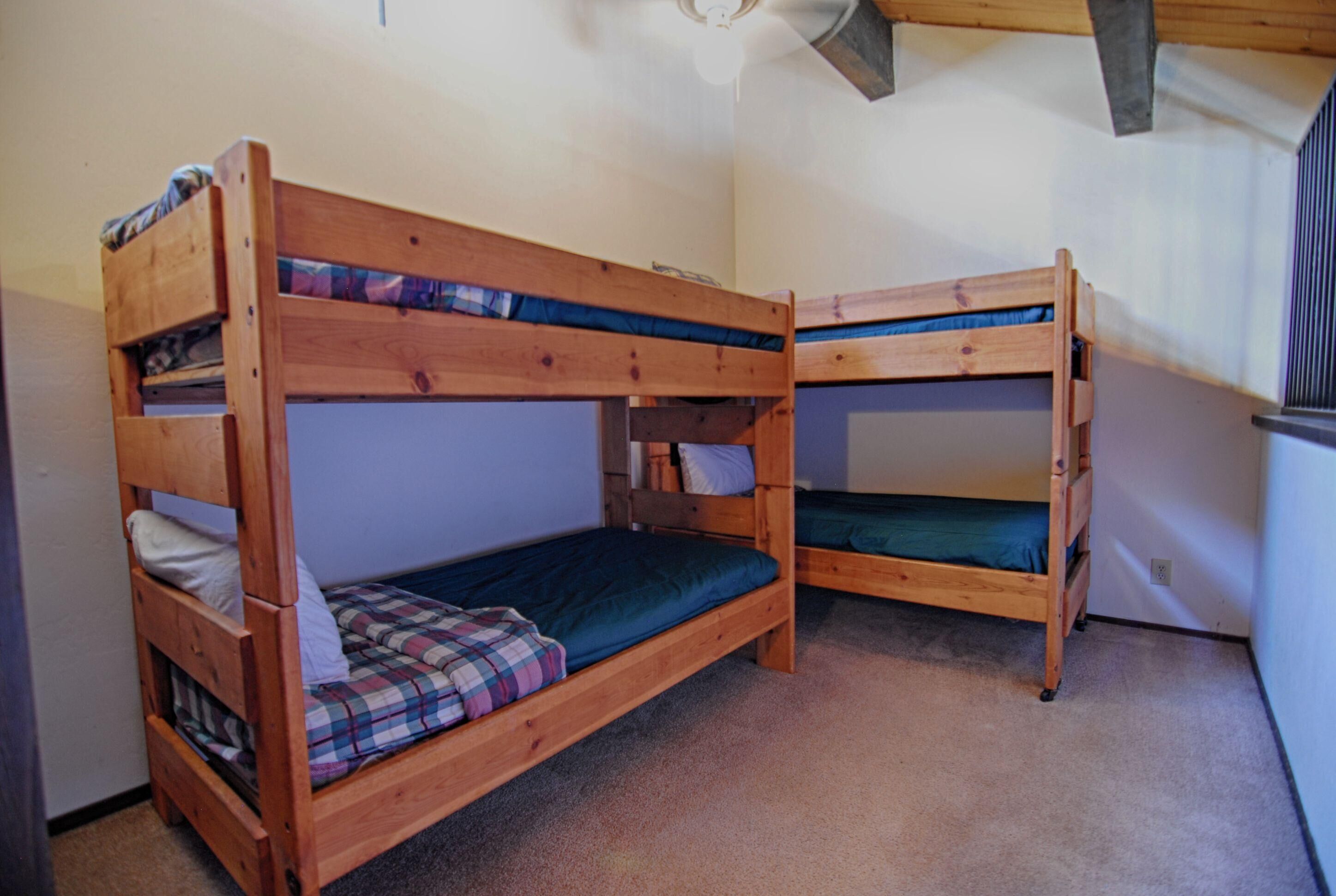 A room with two wooden bunk beds, each with a mattress and pillows.
