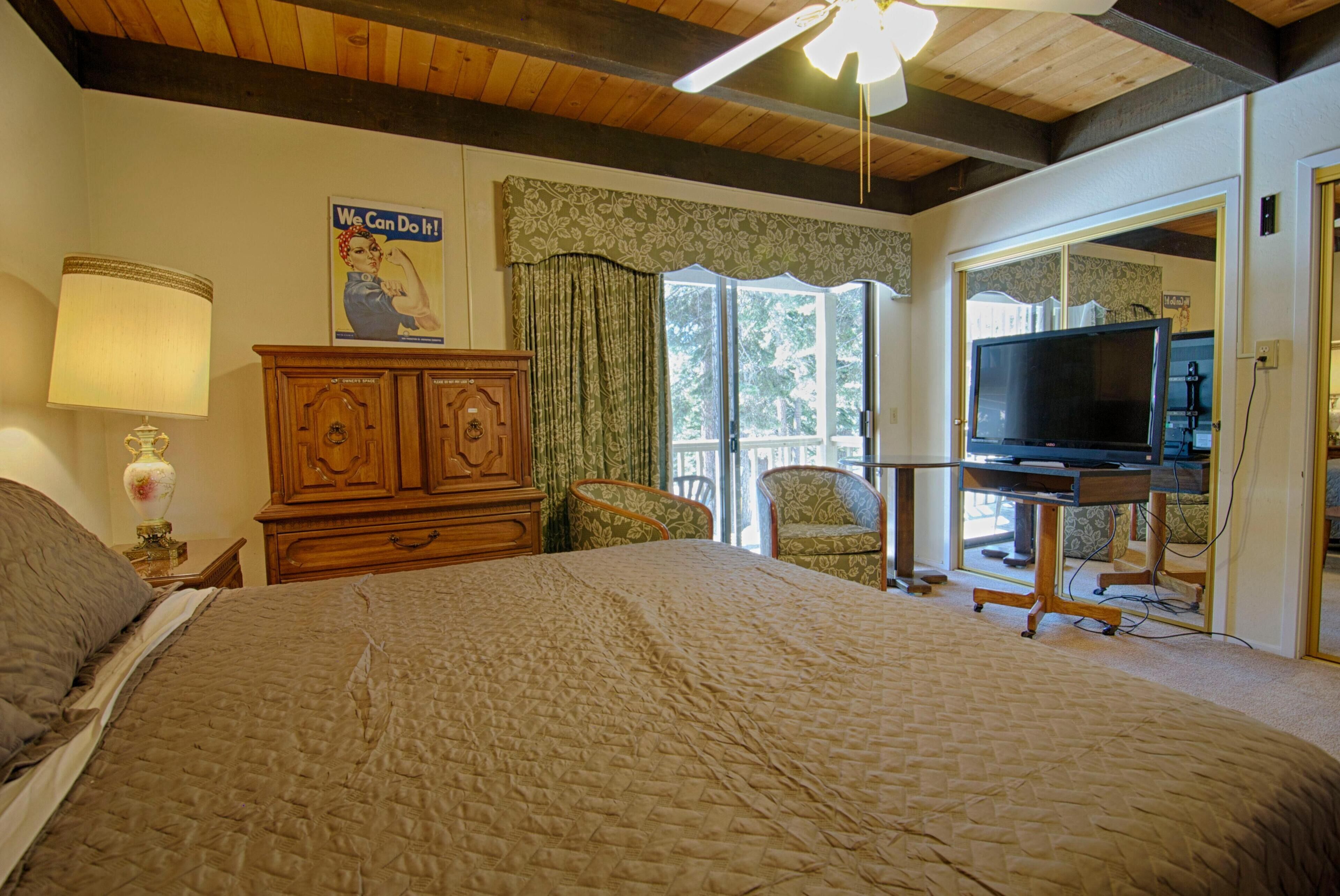 A bedroom with a large bed, a wooden dresser, a television on a stand, and a window with curtains.