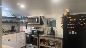 Una cocina equipada con microondas, estufa, horno y refrigerador. Hay estantes con vajilla y una cafetera.