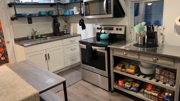 Una cocina moderna con armarios blancos, un microondas negro, una tetera y una cafetera.