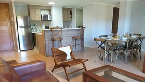A modern living room with a leather sofa, a glass coffee table, and a dining area with wooden chairs and a bar.