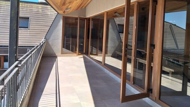 A modern interior with a wooden ceiling, large glass doors, and a balcony with a metal railing.