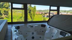 A hot tub on a wooden deck with a view of a green landscape and houses.