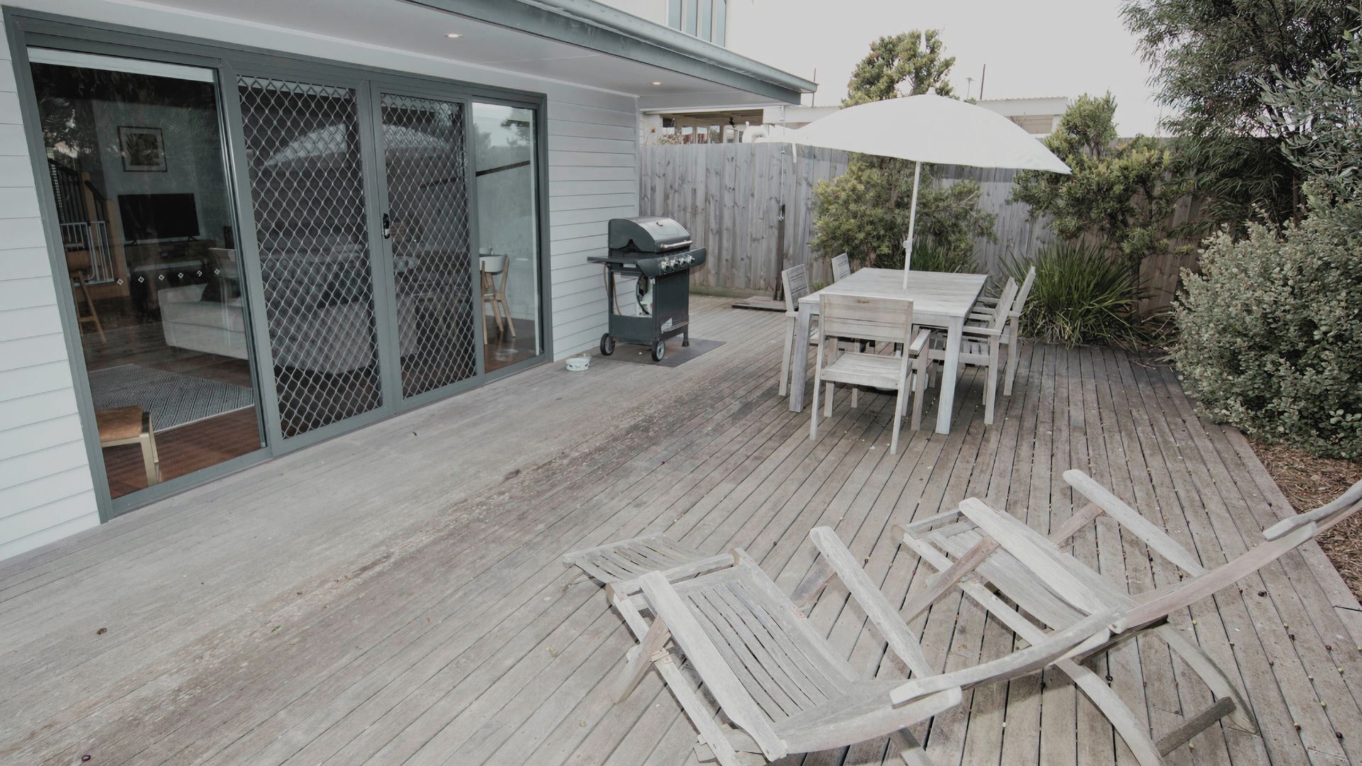 A wooden deck with a table and chairs, a grill, and a white umbrella.