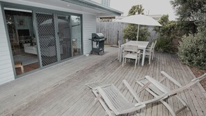 Eine Holzterrasse mit Tisch, Stühlen, einem Grill und einem weißen Sonnenschirm.