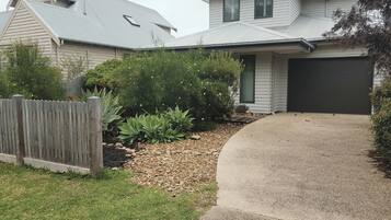 A residential house with a driveway, a wooden fence, and a variety of plants.