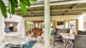 Ein Terrassenbereich im Freien mit Korbmöbeln, einem Esstisch und einem Grill.