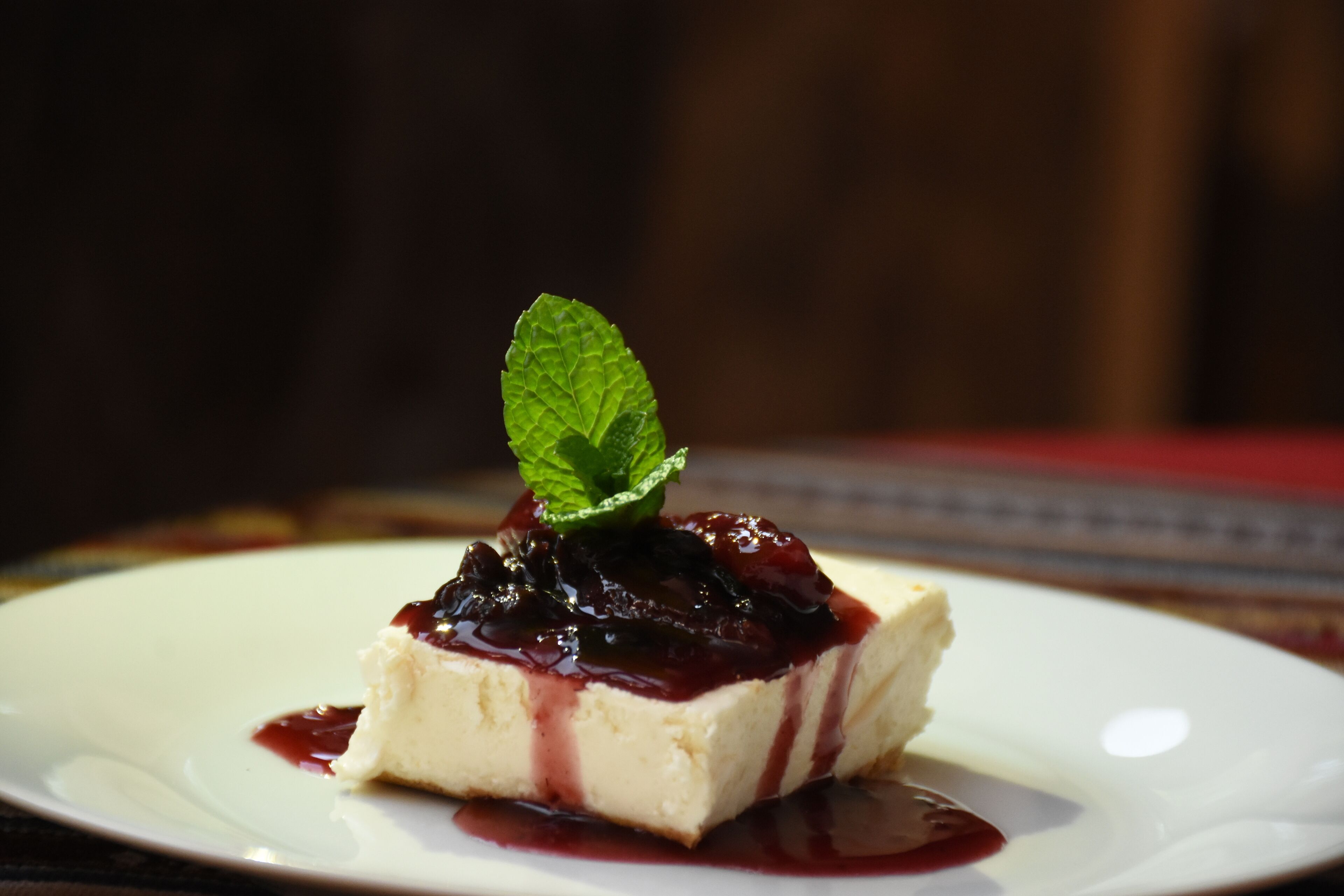 A dessert on a white plate with a dark berry compote and a mint leaf garnish.