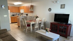 Ein modernes Wohnzimmer mit Essbereich, einer Küche im Hintergrund und einem Fernseher auf einem Schrank.