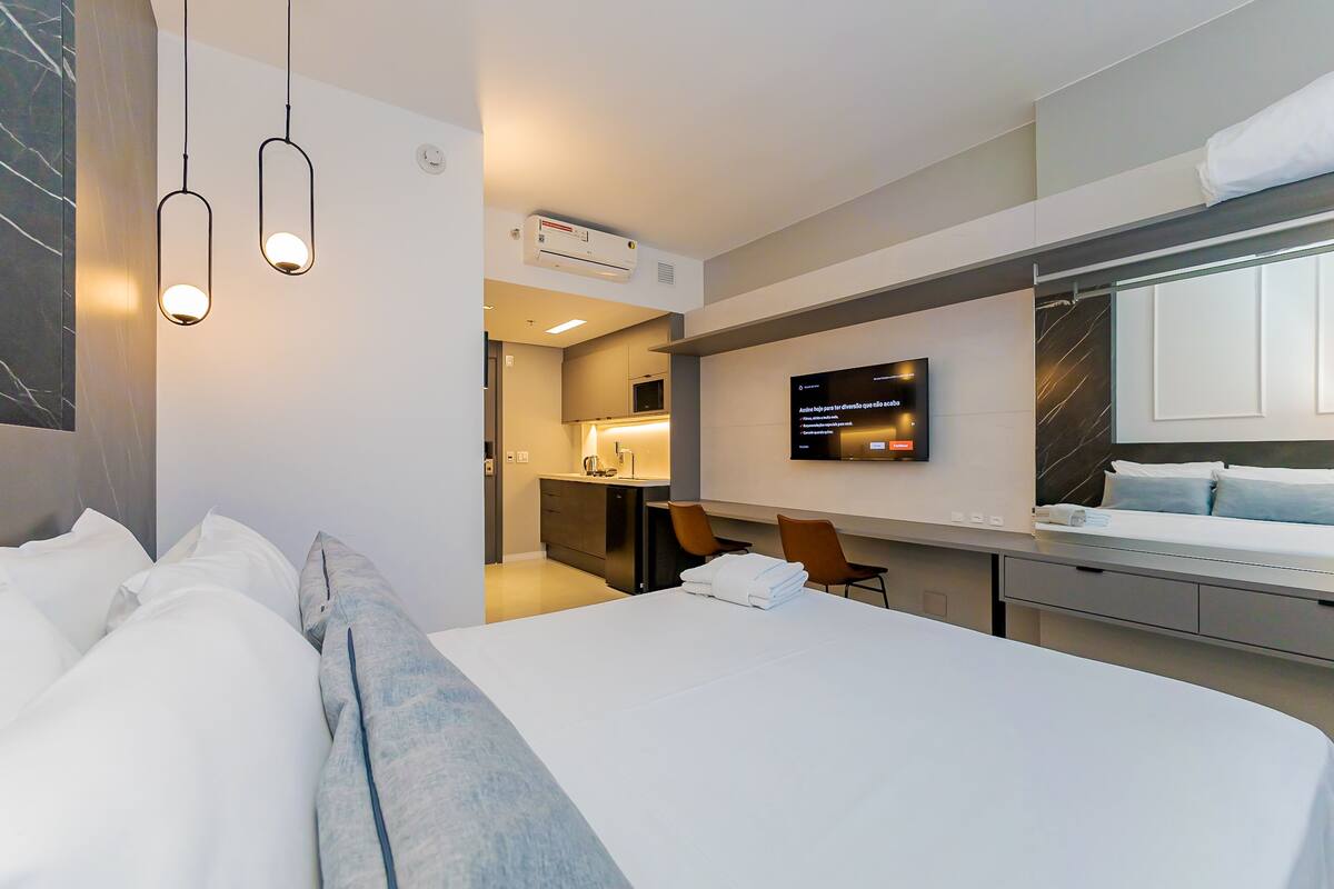 Une chambre d’hôtel moderne avec un lit bien fait, un téléviseur à écran plat fixé au mur et un petit bureau avec une chaise.