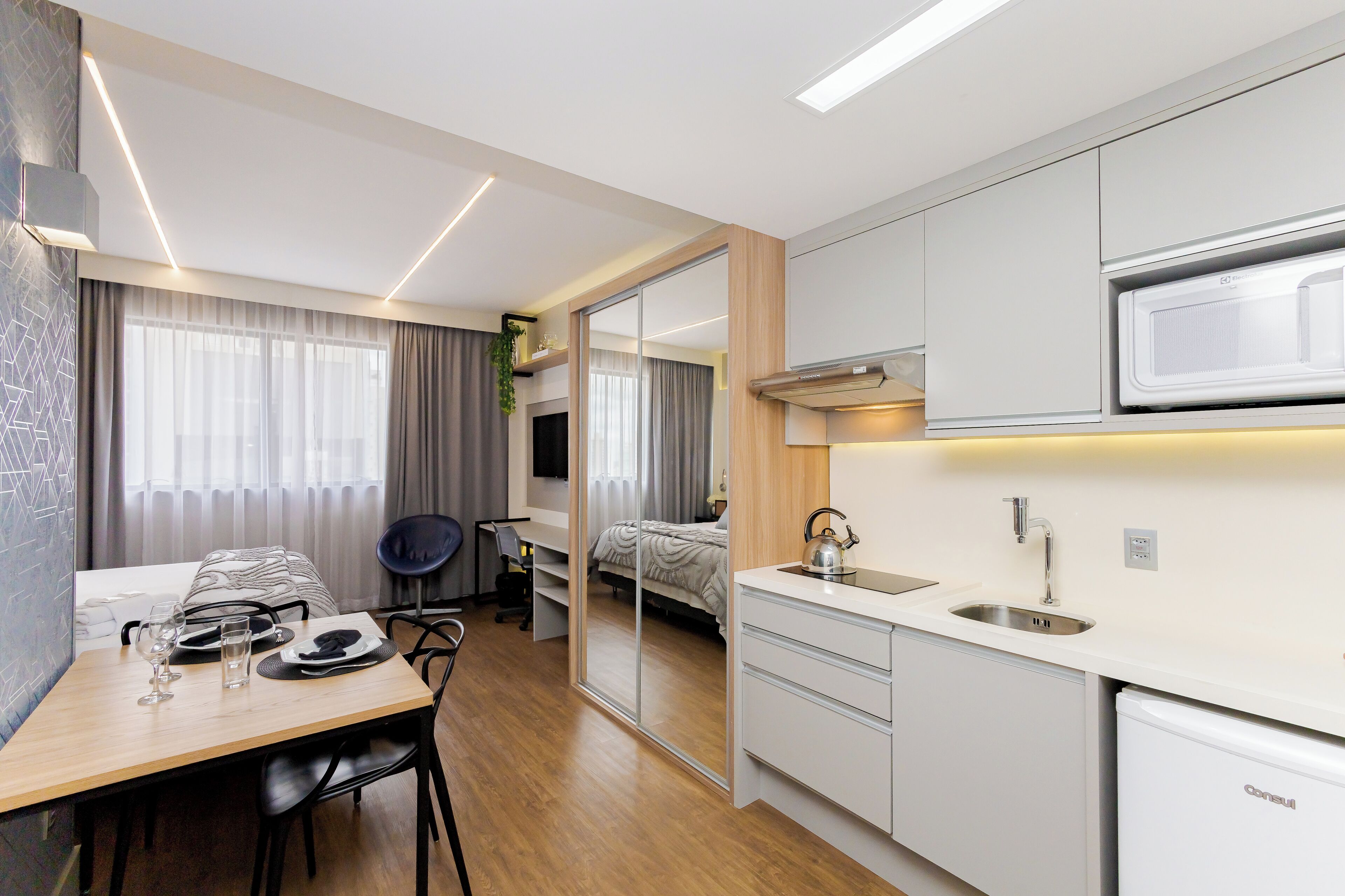 A modern hotel room with a kitchenette, a dining area, and a bed.