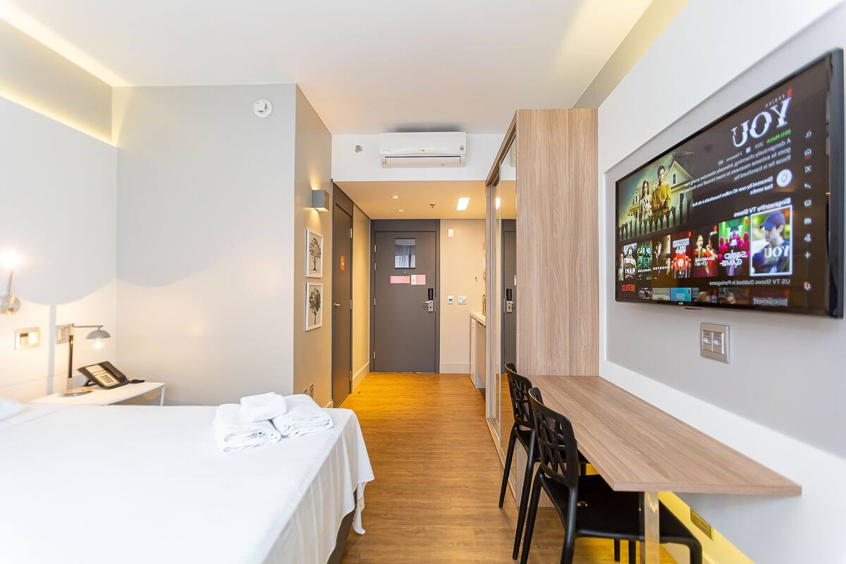 Une chambre d’hôtel avec un lit, un bureau, un téléviseur fixé au mur et un plancher en bois.