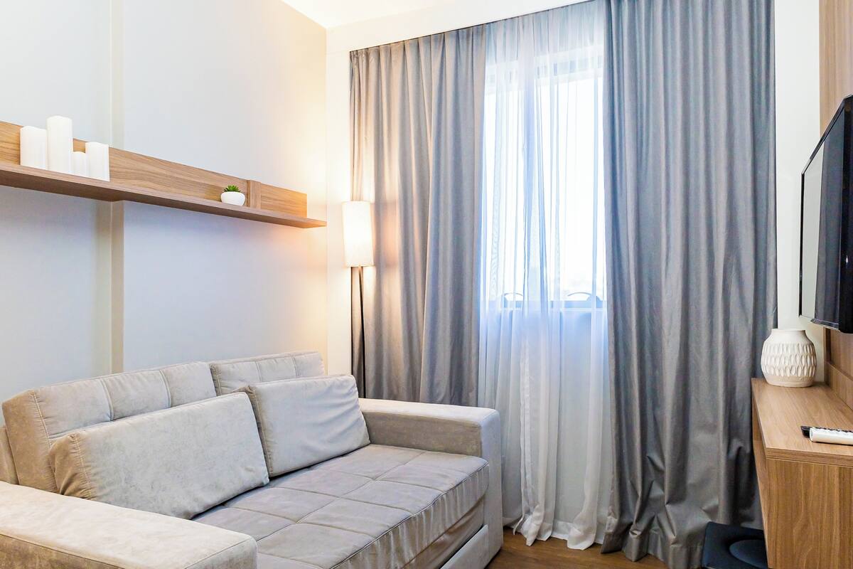 Un salon moderne avec un canapé, un téléviseur, une lampe et une fenêtre avec des rideaux.