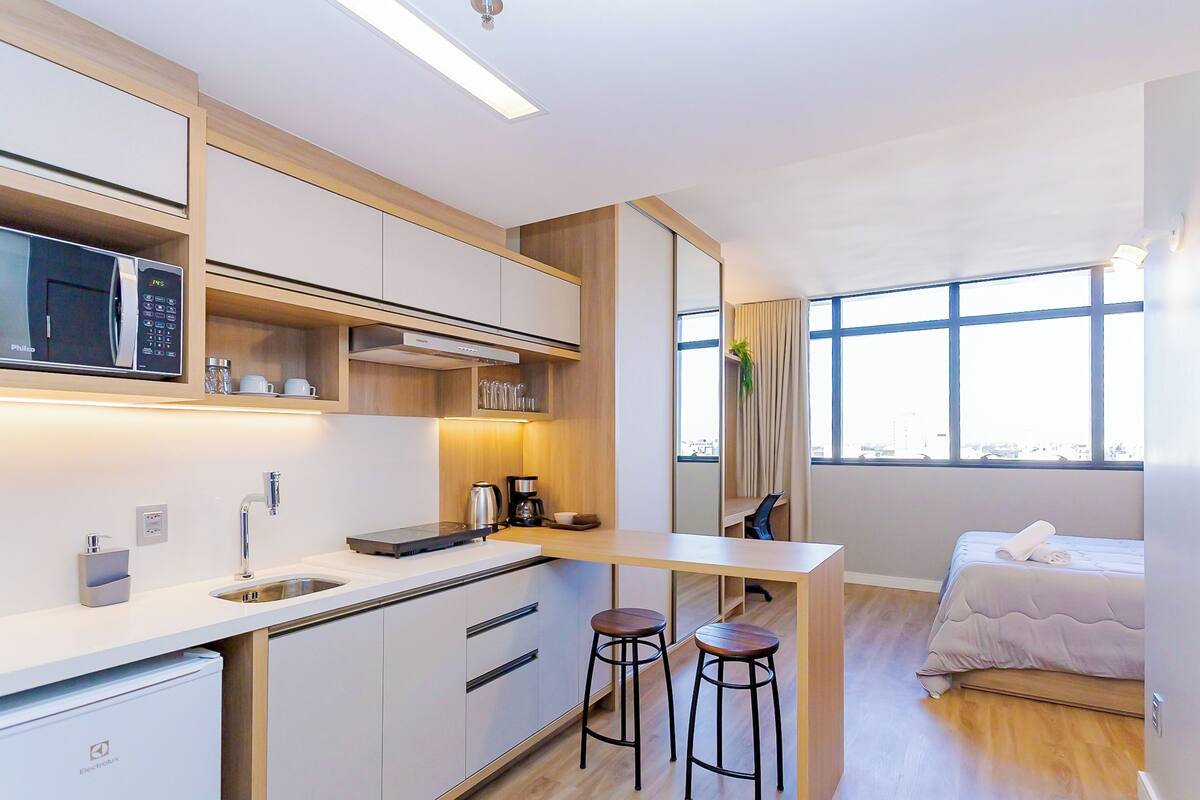 Une chambre d’hôtel compacte dotée d’une kitchenette, d’un lit avec vue et d’un petit coin salon.