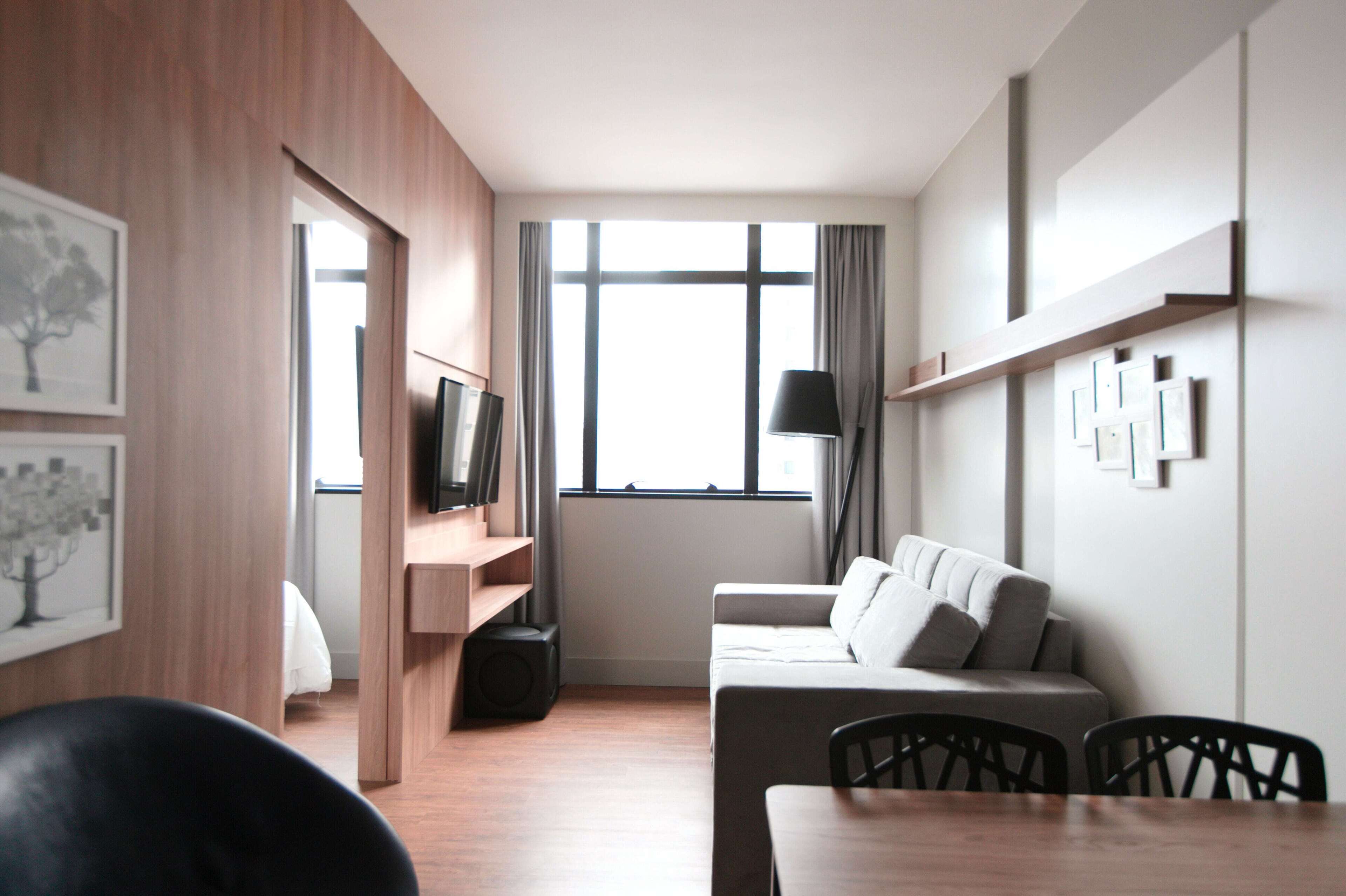 A modern hotel room with a wooden floor, a sofa, a dining table, and a TV.