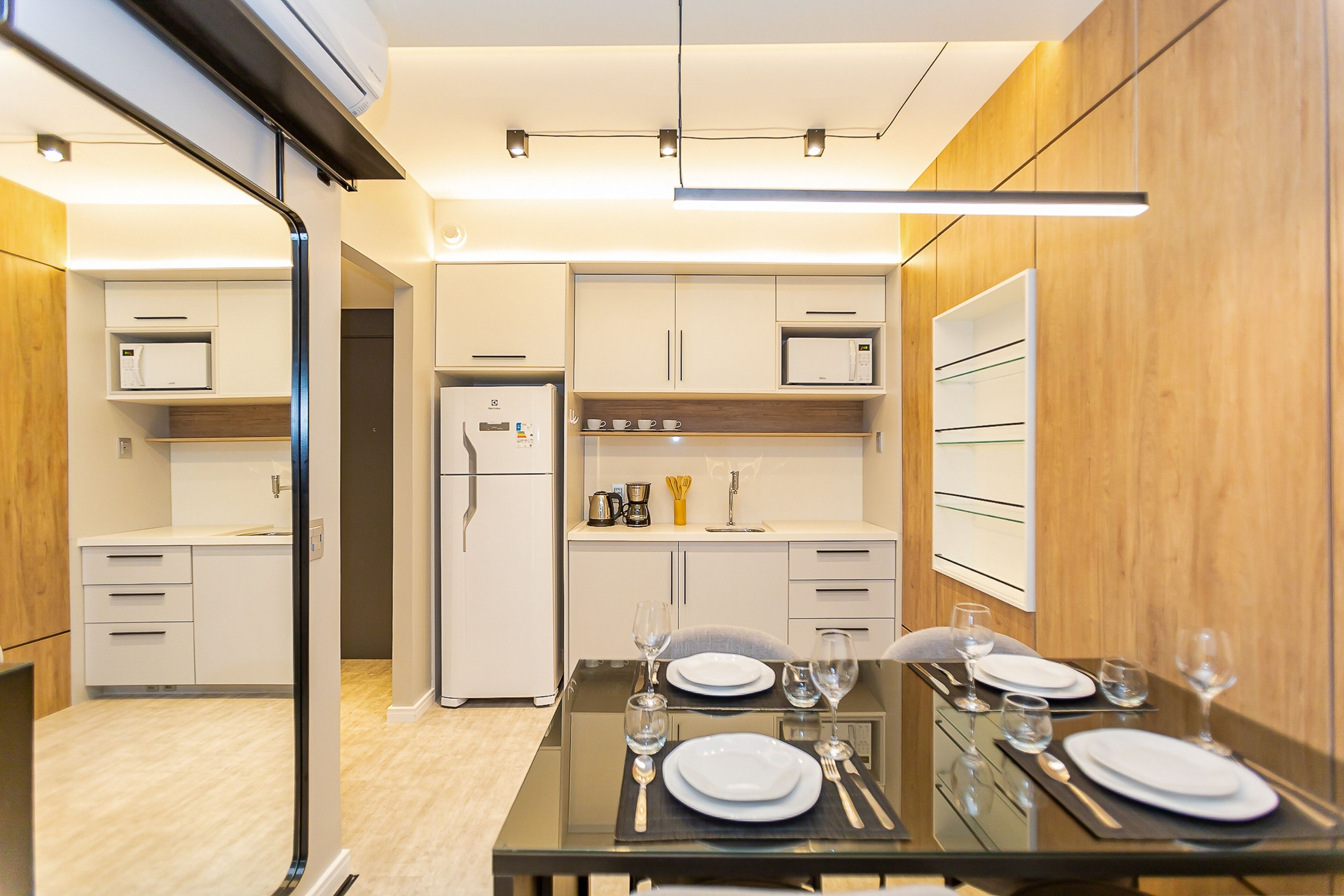 A modern kitchen with white cabinets, a refrigerator, and a dining area set for two with a glass table and white plates.