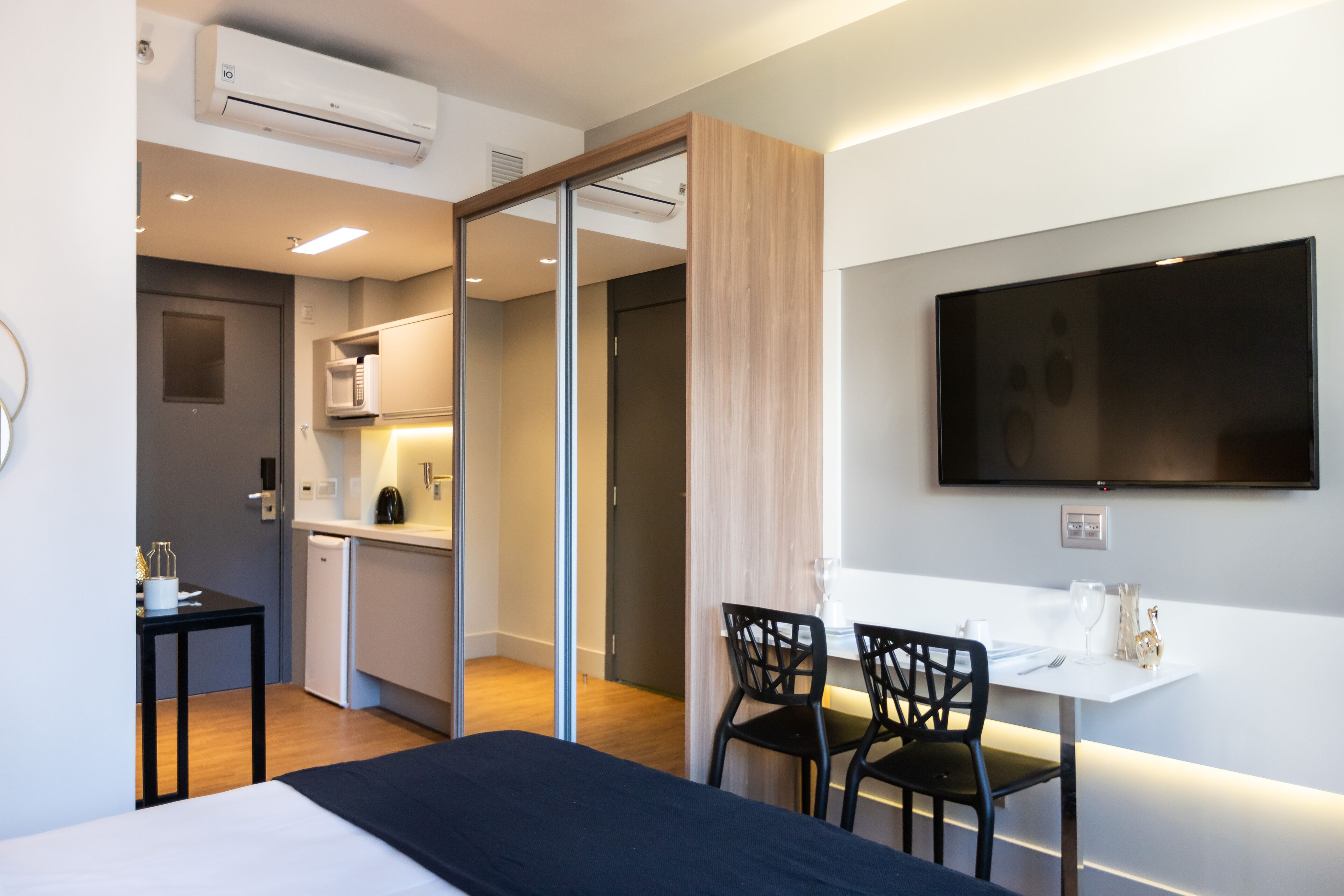 A modern hotel room with a bed, a desk, a chair, a dining table, and a TV.