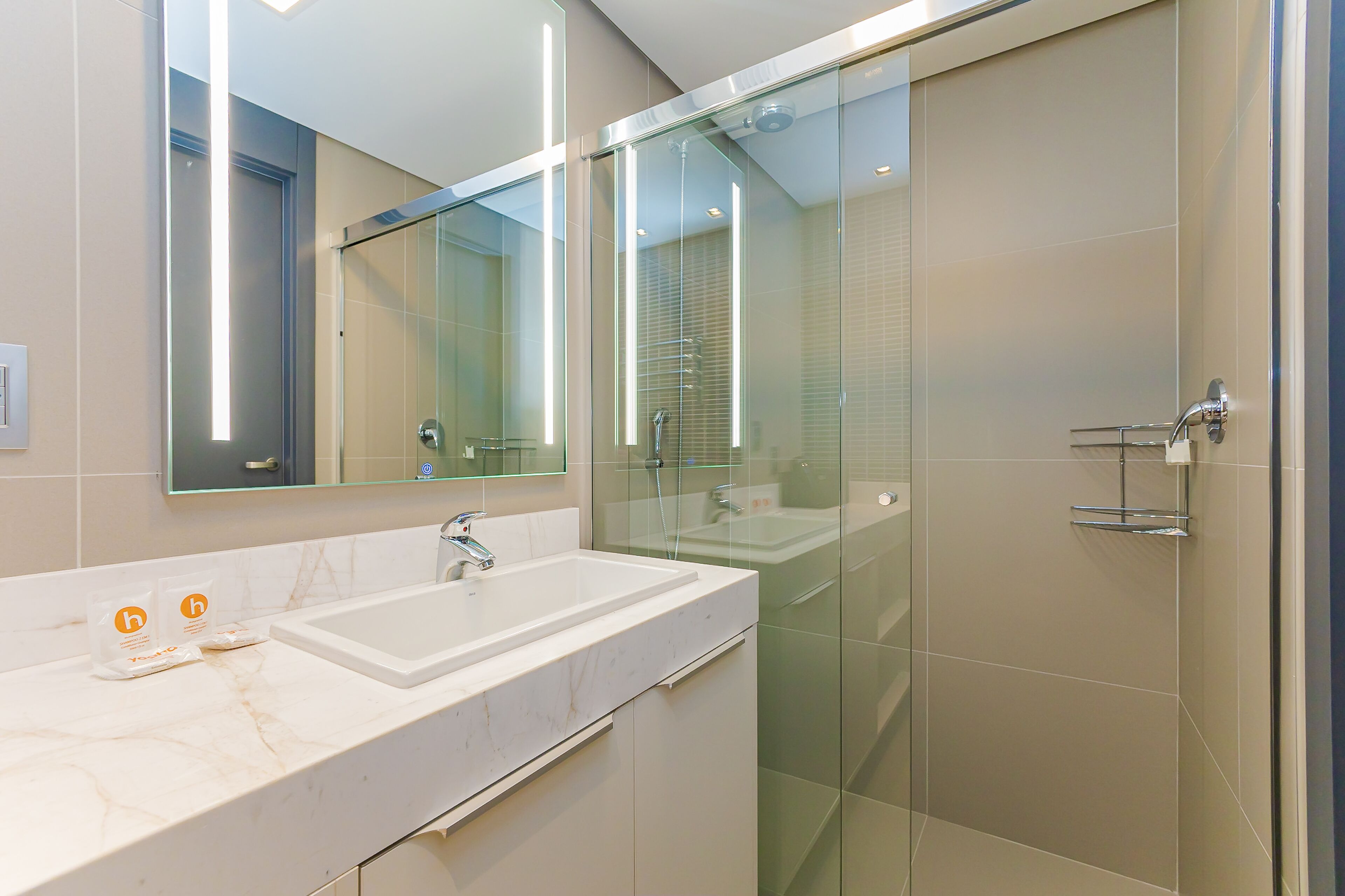 Un baño moderno con cabina de ducha de vidrio, lavamanos de mármol blanco y un espejo grande.