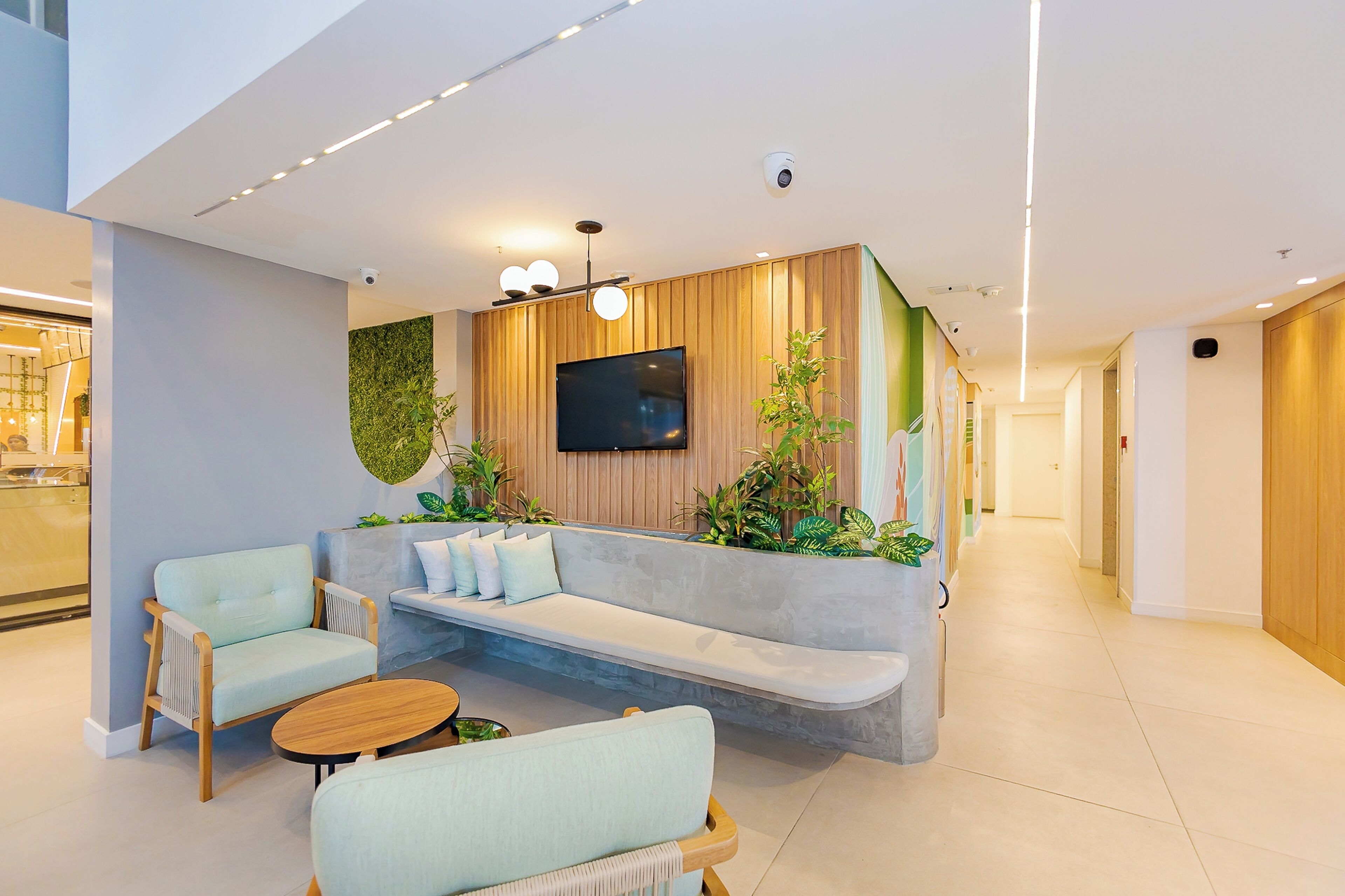 A modern lobby with a seating area, a flat-screen TV, and a green wall with plants.