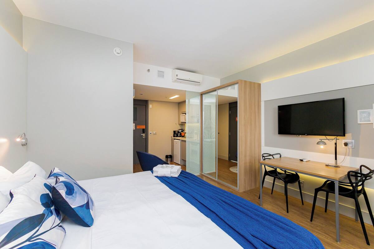 Une chambre d’hôtel équipée d’un lit, d’un bureau, d’une télévision et d’une salle de bain, le tout visible à travers une porte coulissante.