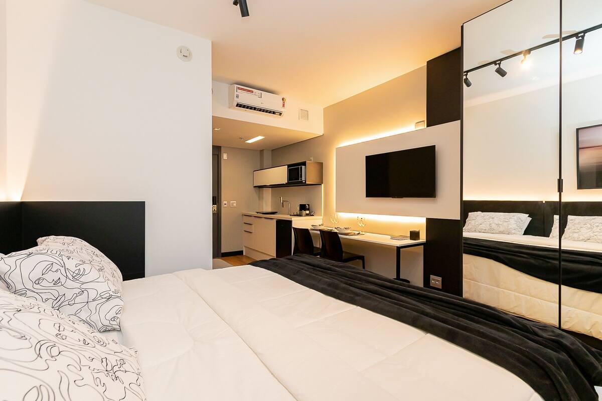 Une chambre d’hôtel moderne équipée d’un lit, d’un bureau, d’une télévision à écran plat et d’une kitchenette.