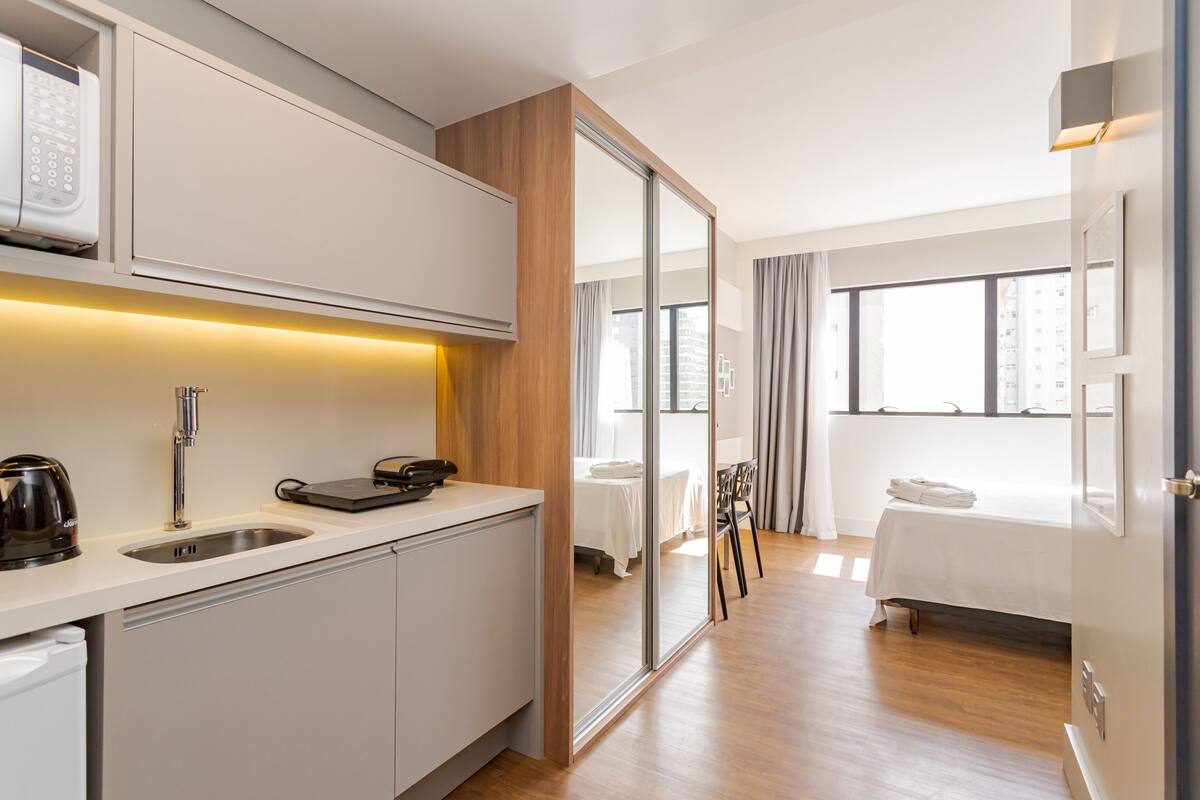 Une chambre d’hôtel moderne dotée d’une kitchenette, d’un lit, d’un coin repas et offrant une vue sur la ville.