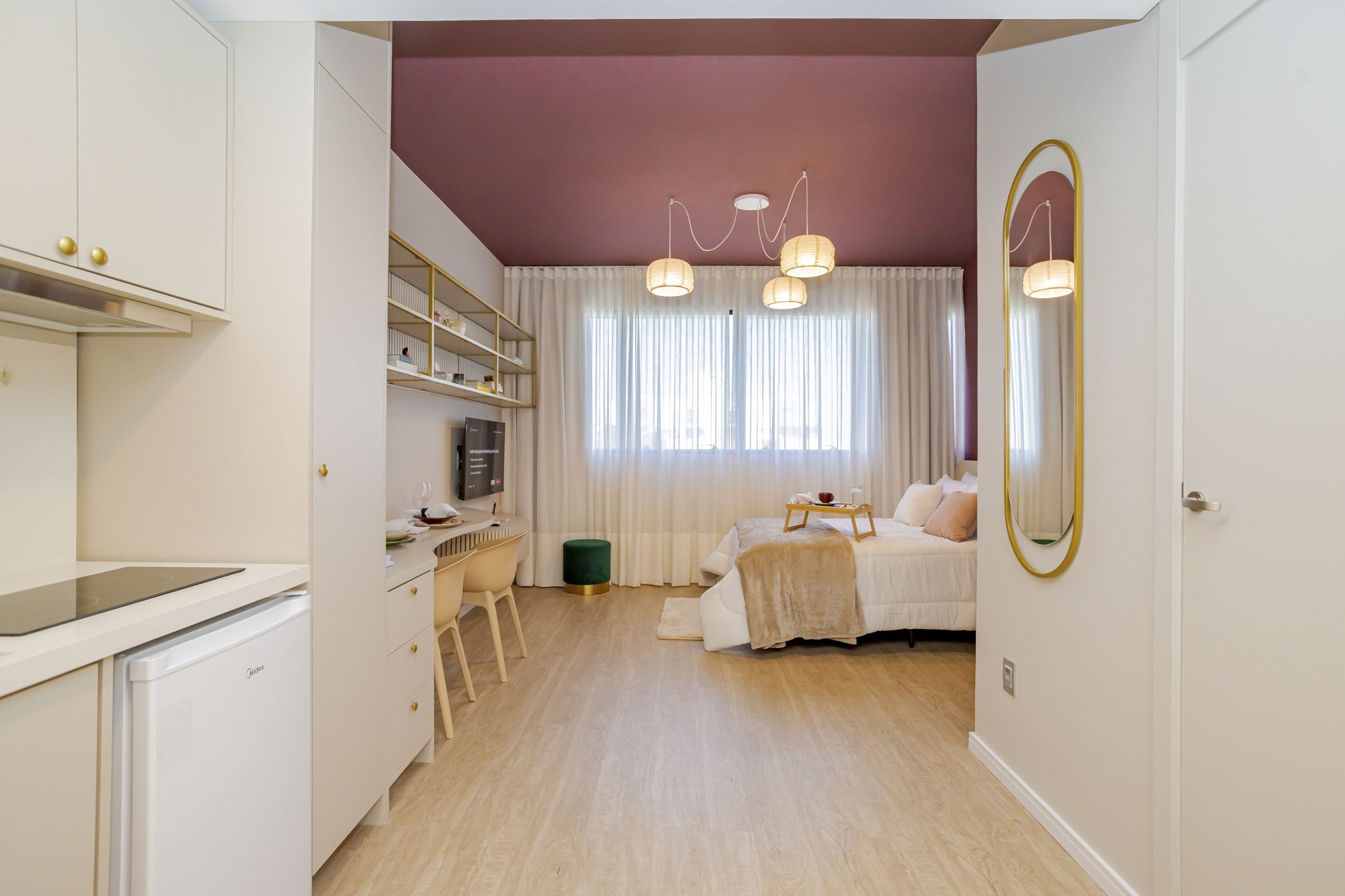 Un dormitorio con cama, mesita de noche y un espejo grande. Hay una ventana con cortinas y una lámpara en el techo.