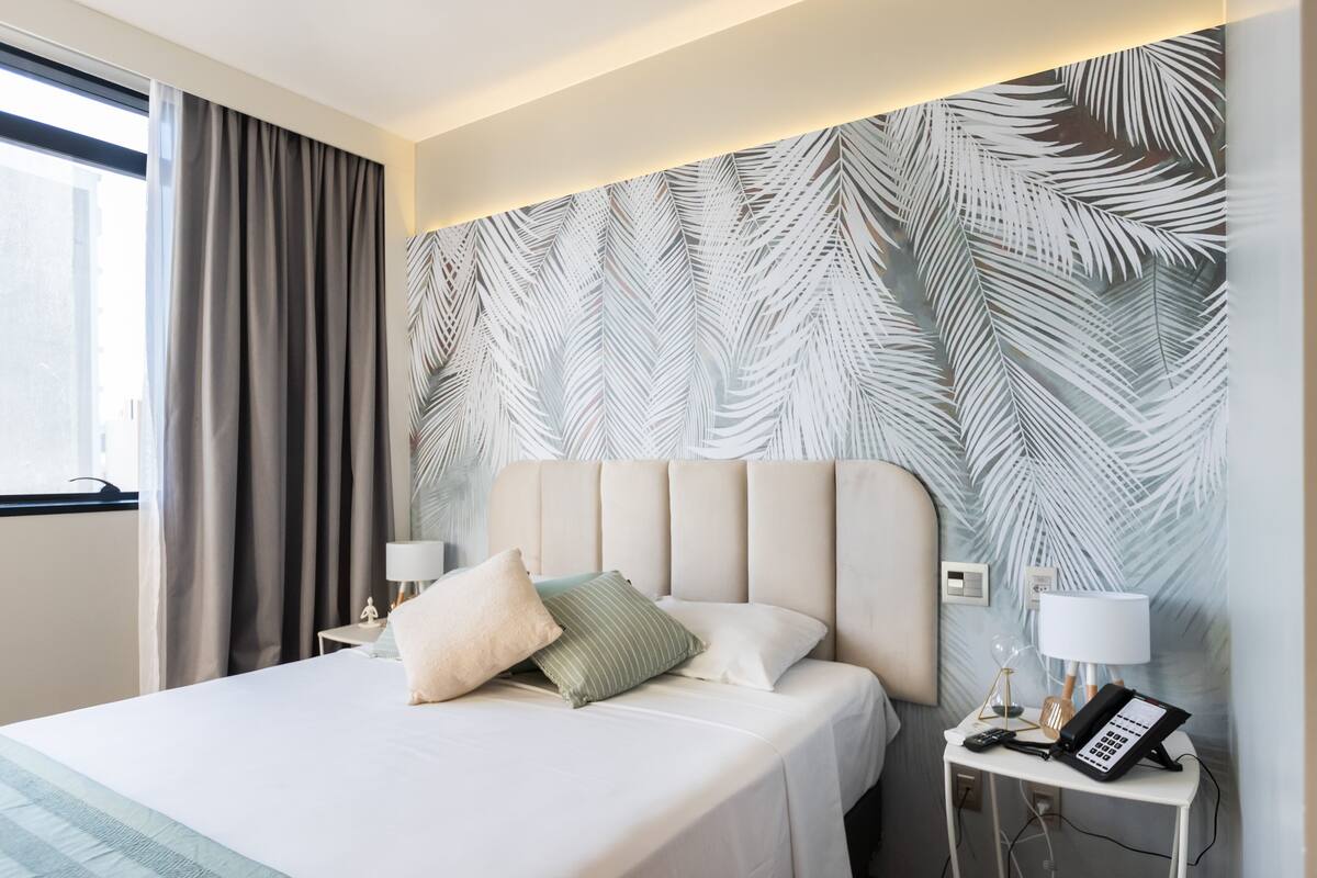 Une chambre d’hôtel comprenant un lit, une table de chevet, un téléphone et un mur orné d’un motif de feuilles.