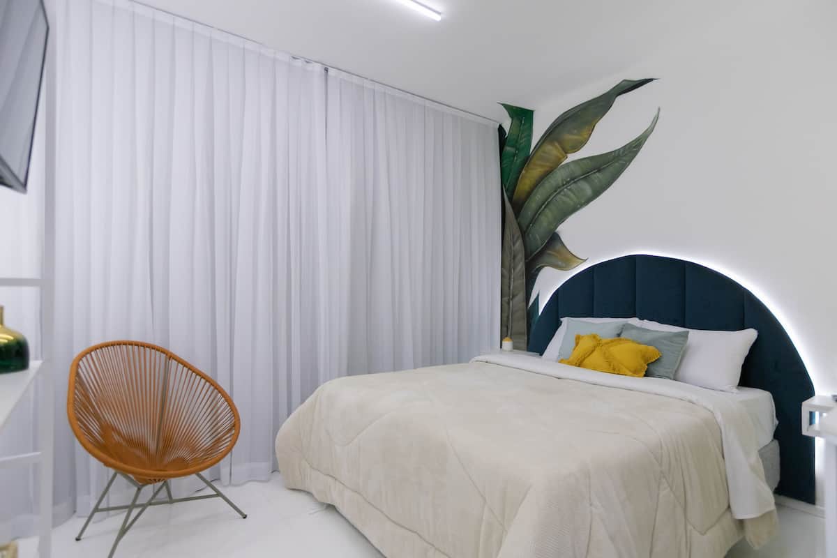 Une chambre à coucher avec un lit, une chaise et une grande plante.