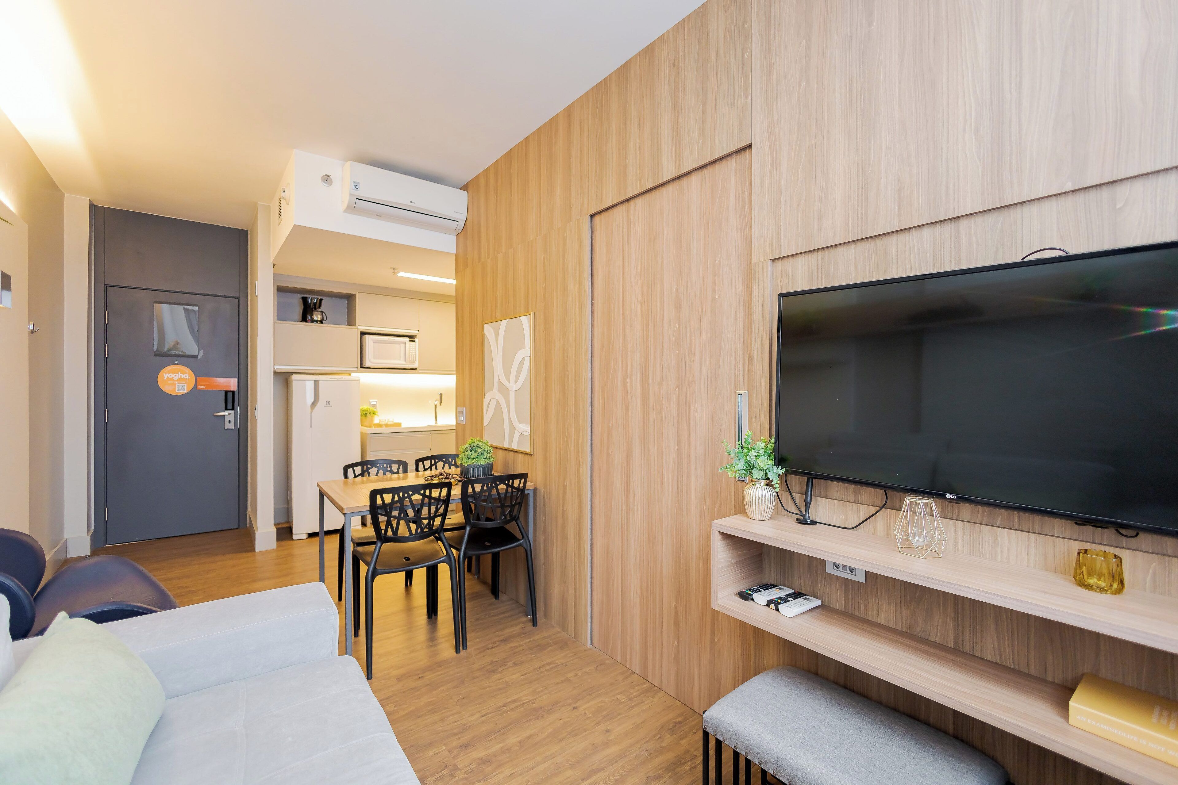 Una camera d'albergo moderna con una grande televisione a schermo piatto, un'area pranzo con tavolo e sedie, e un angolo cottura.