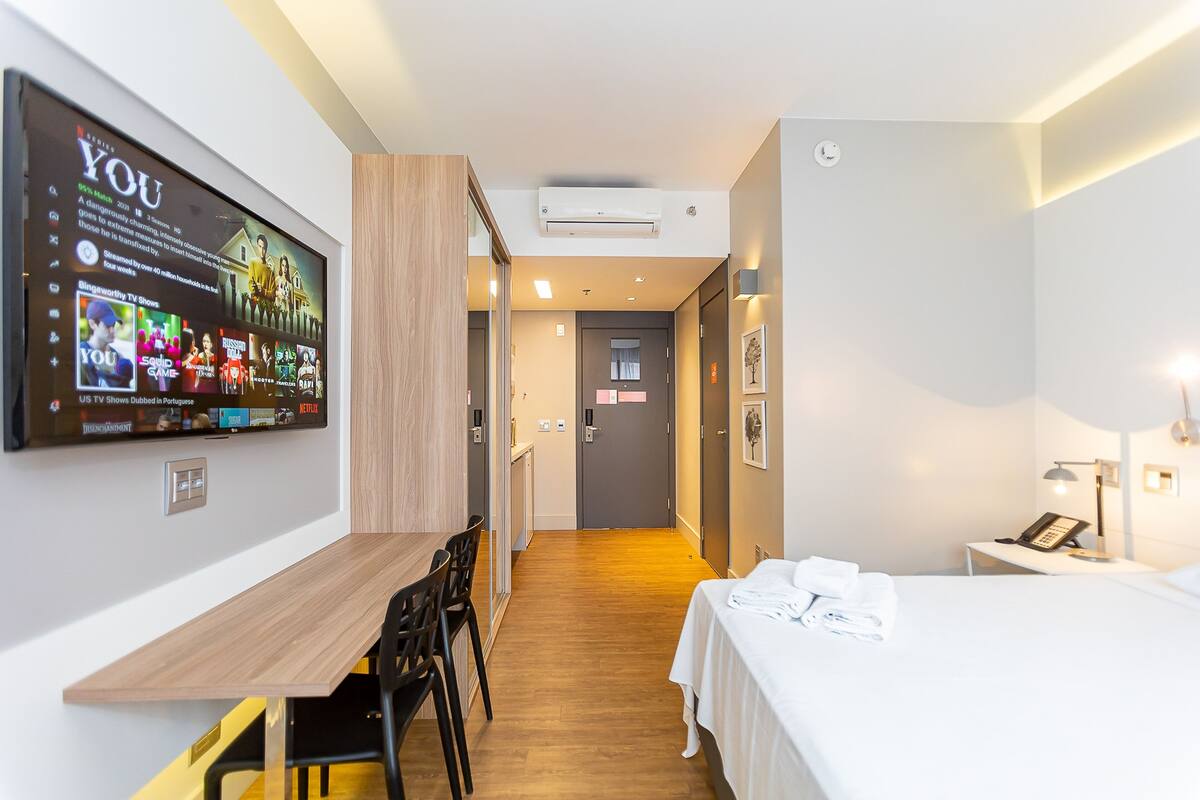 Une chambre d’hôtel comprenant un lit, un bureau avec des chaises, un téléviseur fixé au mur et une porte donnant sur une autre pièce.