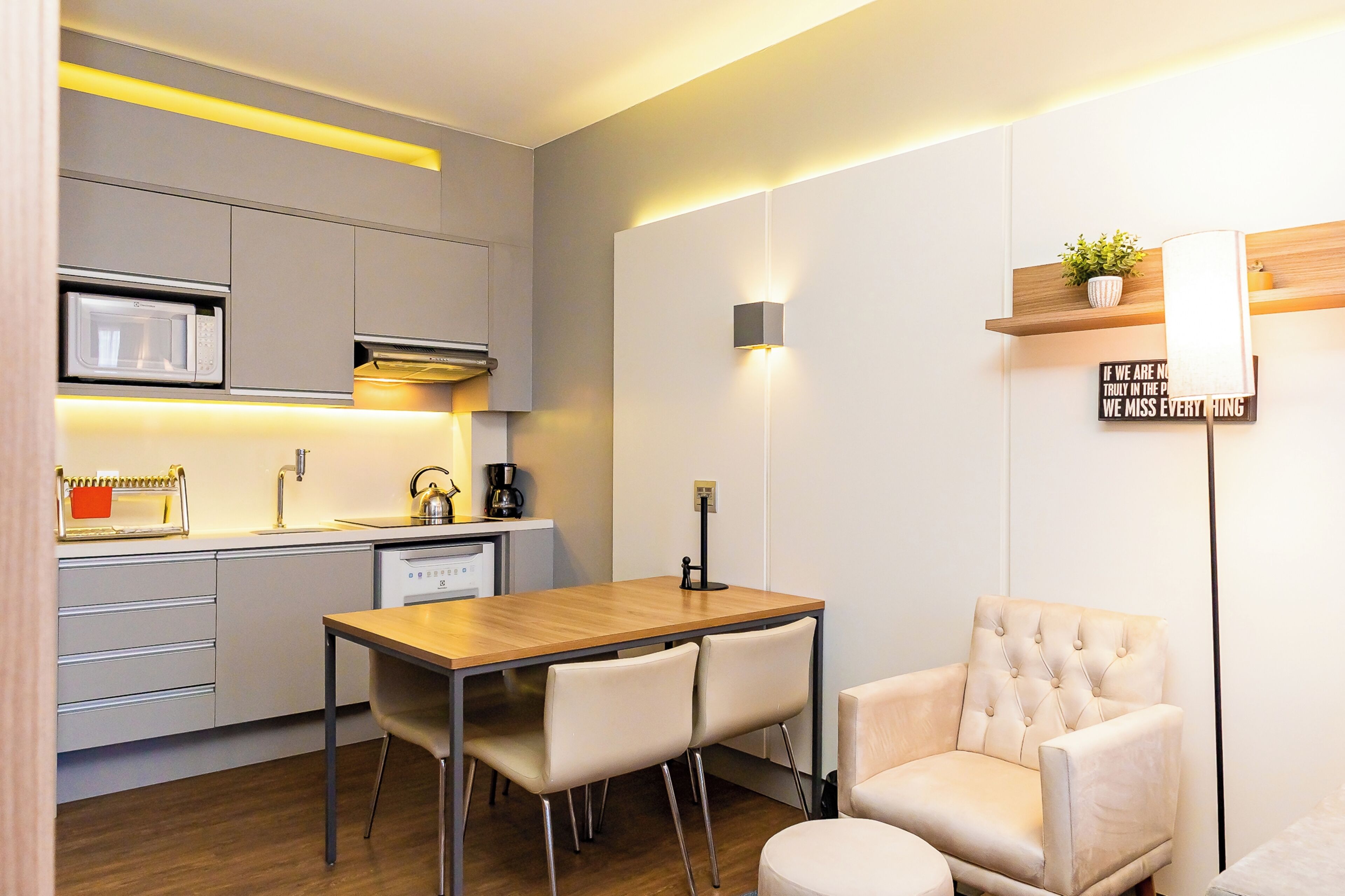 A modern kitchen with a wooden dining table, white chairs, and a tufted armchair.