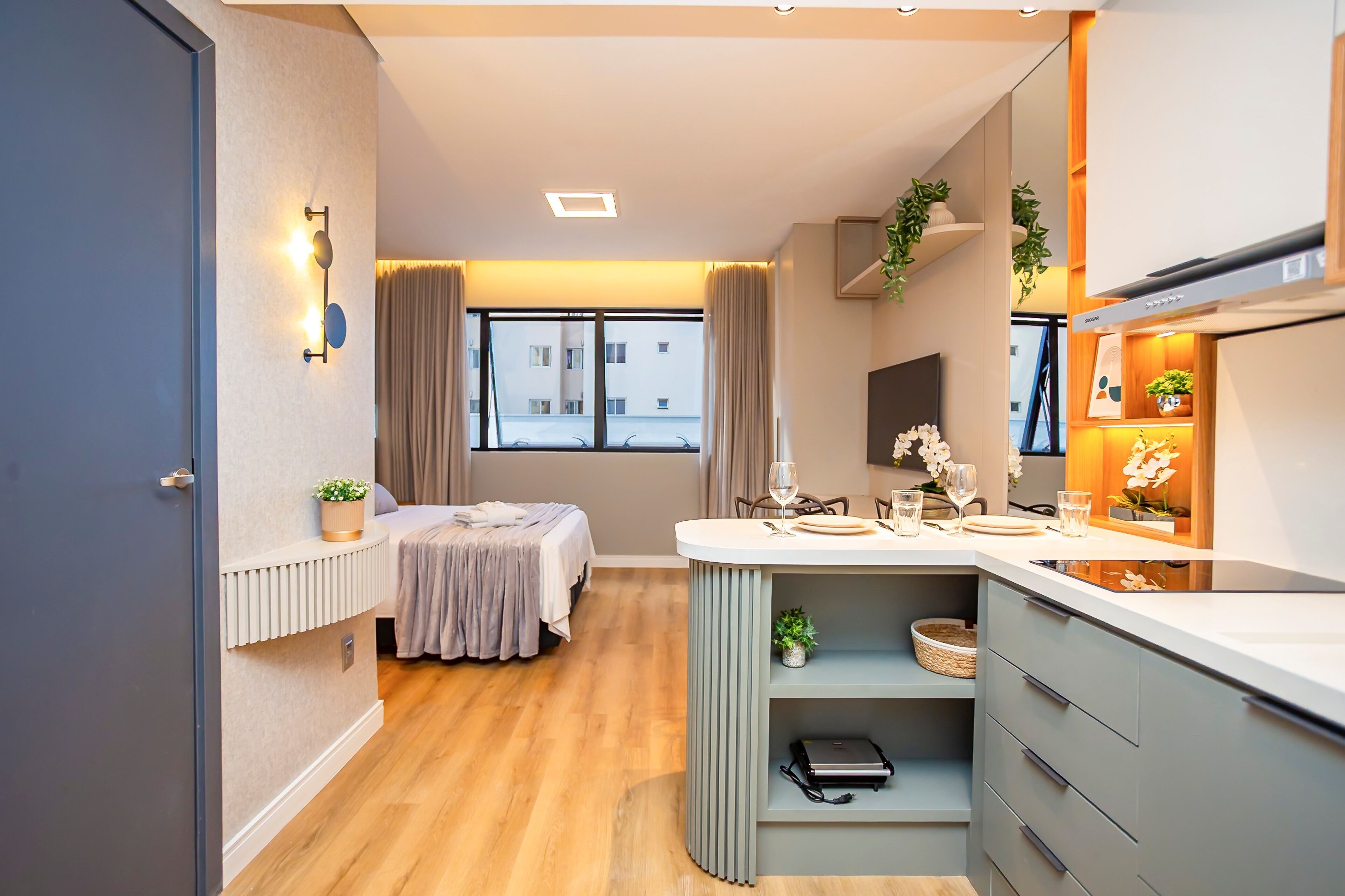 A modern hotel room with a bed, bedside table, and a small kitchenette.