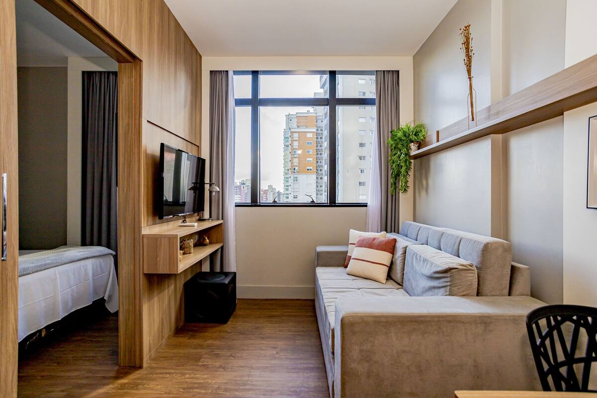 Une chambre d’hôtel compacte comprenant un lit, un canapé, une télévision et une fenêtre donnant sur la ville.