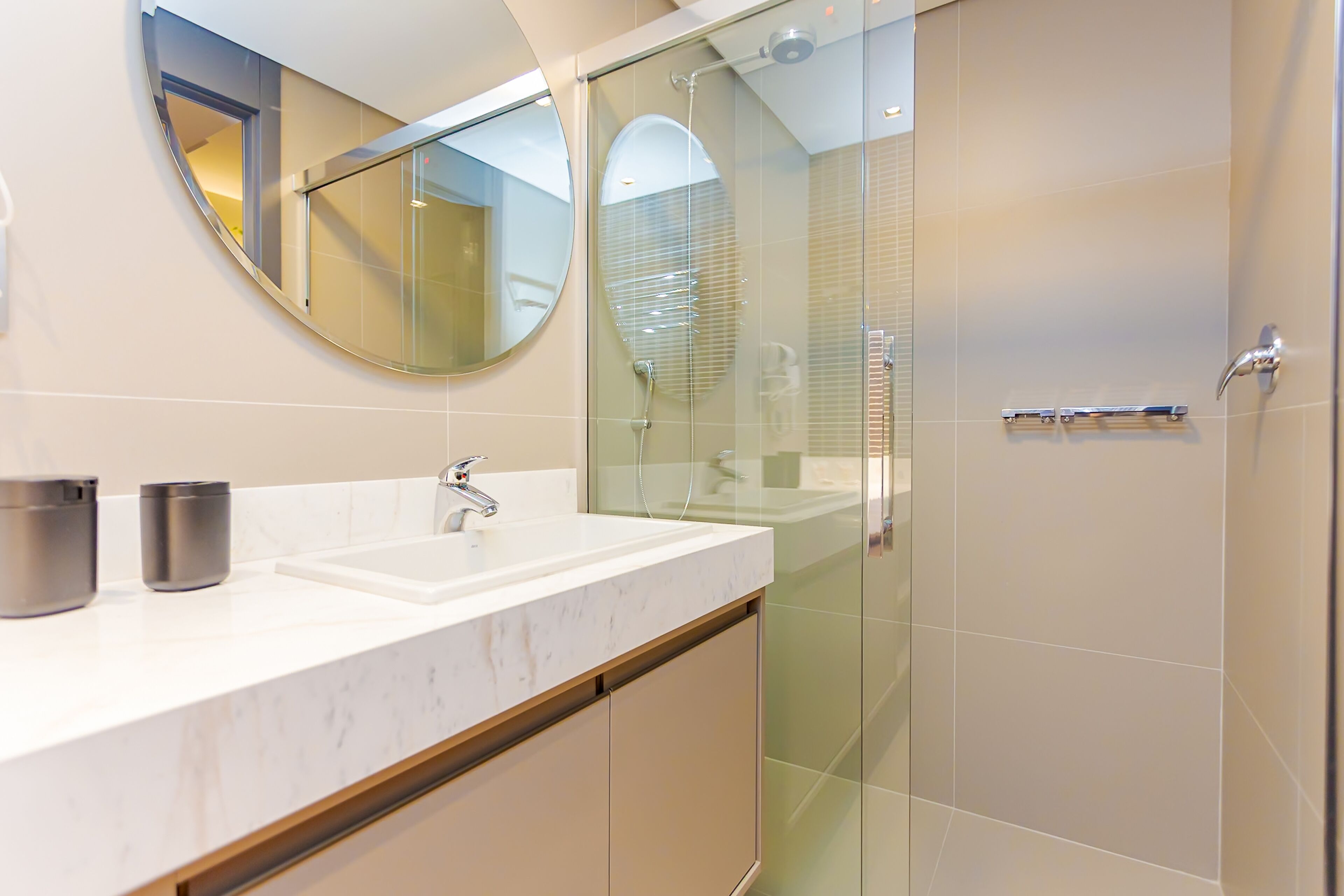 Un bagno moderno con un lavabo in marmo bianco, una cabina doccia in vetro e un grande specchio sopra il lavabo.