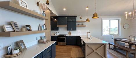 A modern kitchen with dark blue cabinets, a central island, and pendant lighting.
