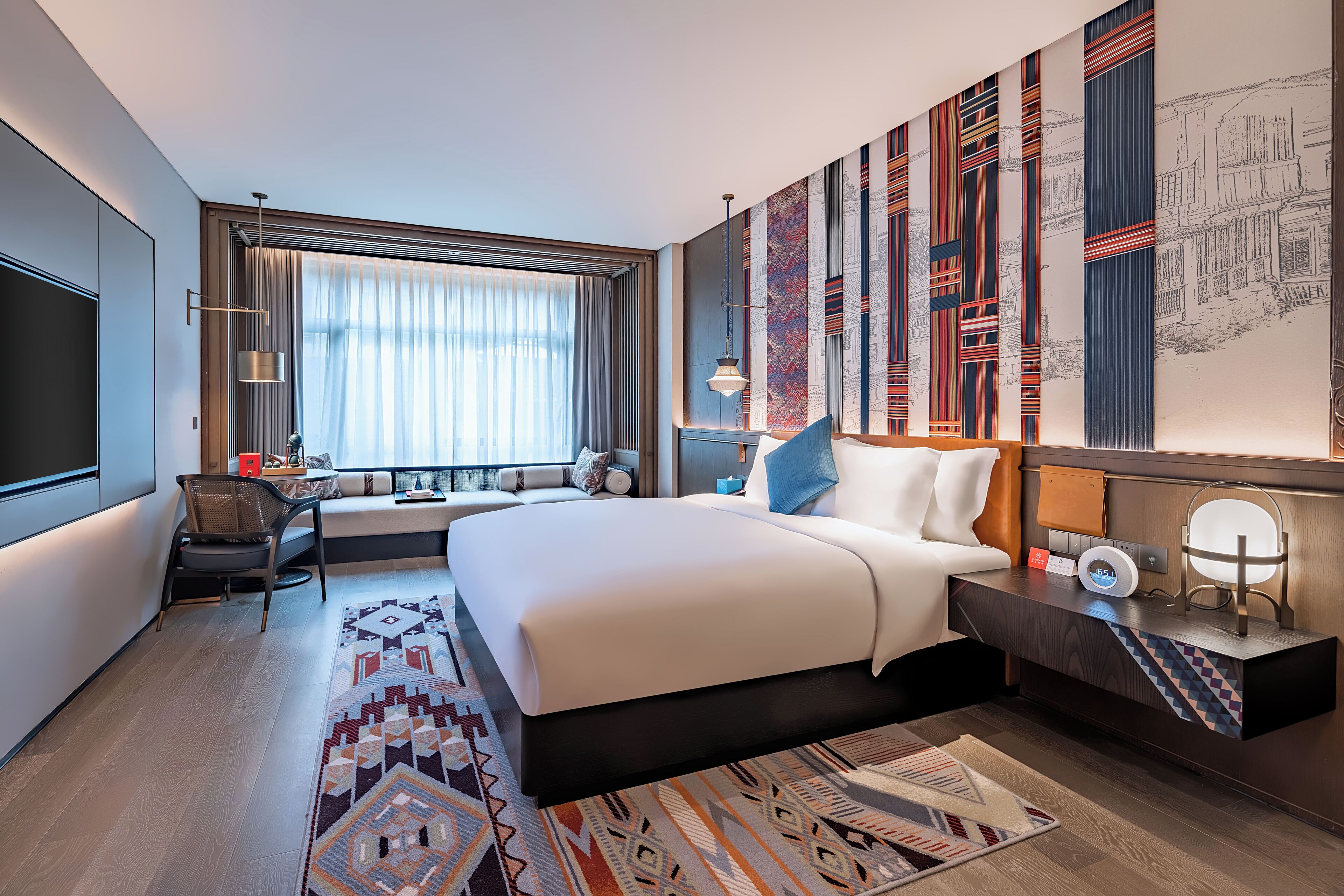 A modern hotel room with a large bed, a desk, and a seating area by the window.