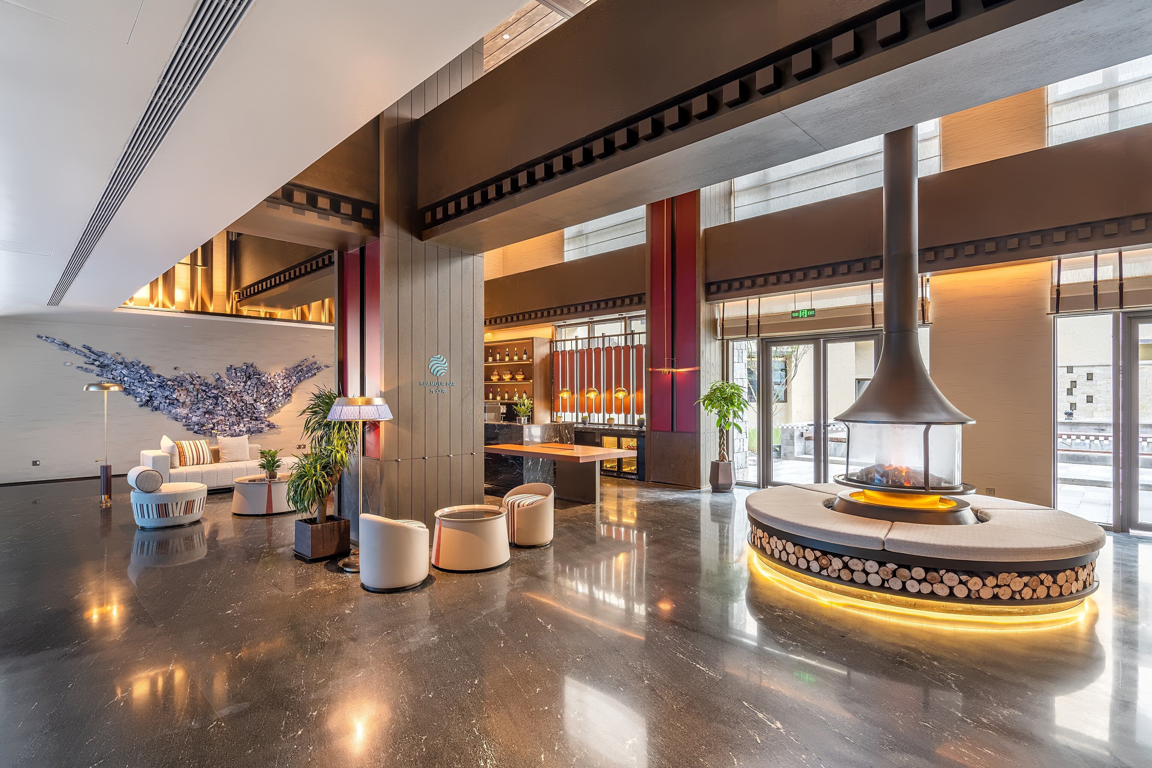 A spacious lobby with a polished floor, seating areas, a central fire feature, and a decorative wall.