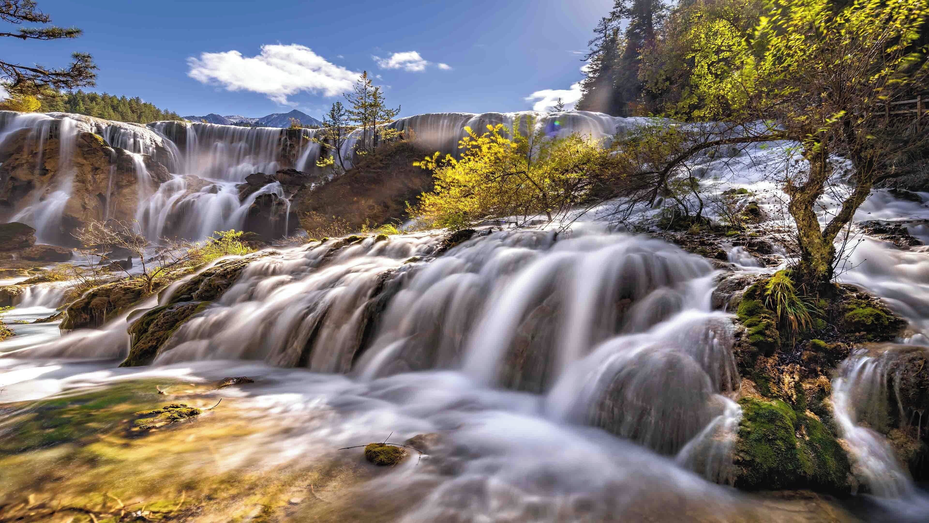 Una cascada con múltiples saltos de agua rodeada de árboles y rocas.