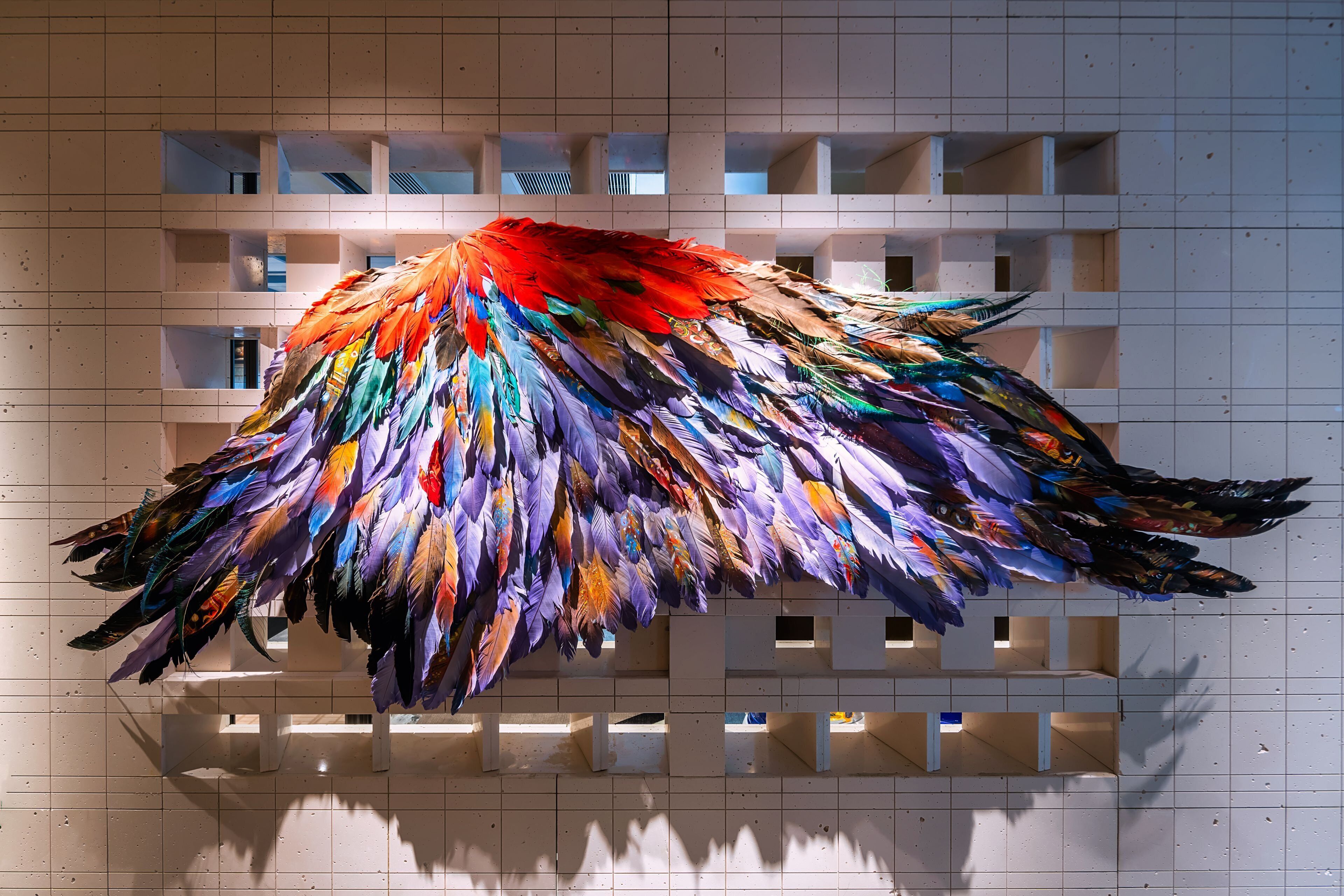 A colorful feather installation against a tiled wall with a grid pattern.